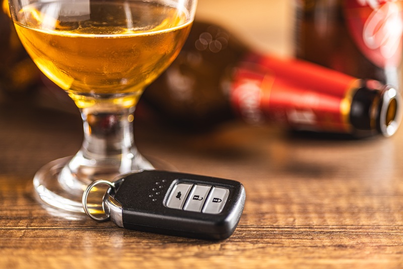 A car key, empty beer bottles, and glass of alcohol sit on a wooden table, signifying the dangers of drinking and driving.